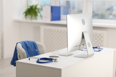 Photo of Doctor's workplace with stethoscope, paperwork and computer on desk. Space for text