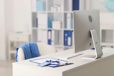 Photo of Doctor's workplace with stethoscope, paperwork and computer on desk. Space for text