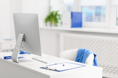 Photo of Doctor's workplace with computer and paperwork on desk. Space for text