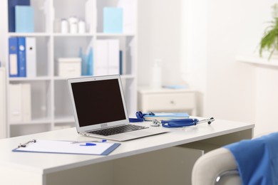 Photo of Doctor's workplace with stethoscope, paperwork and laptop on desk