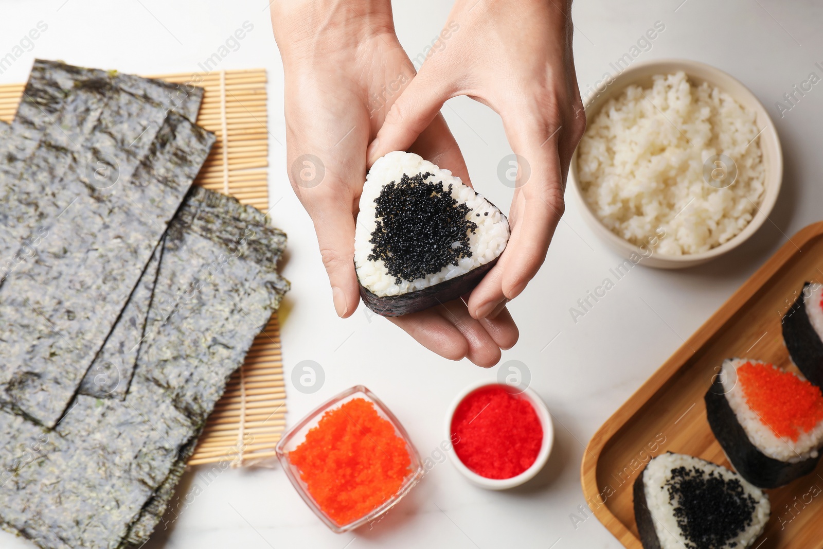 Woman with tasty tobiko onigiri (Japanese rice balls) at white marble table, top view Photo of Woman with tasty tobiko onigiri (Japanese rice balls) at white marble table, top view
