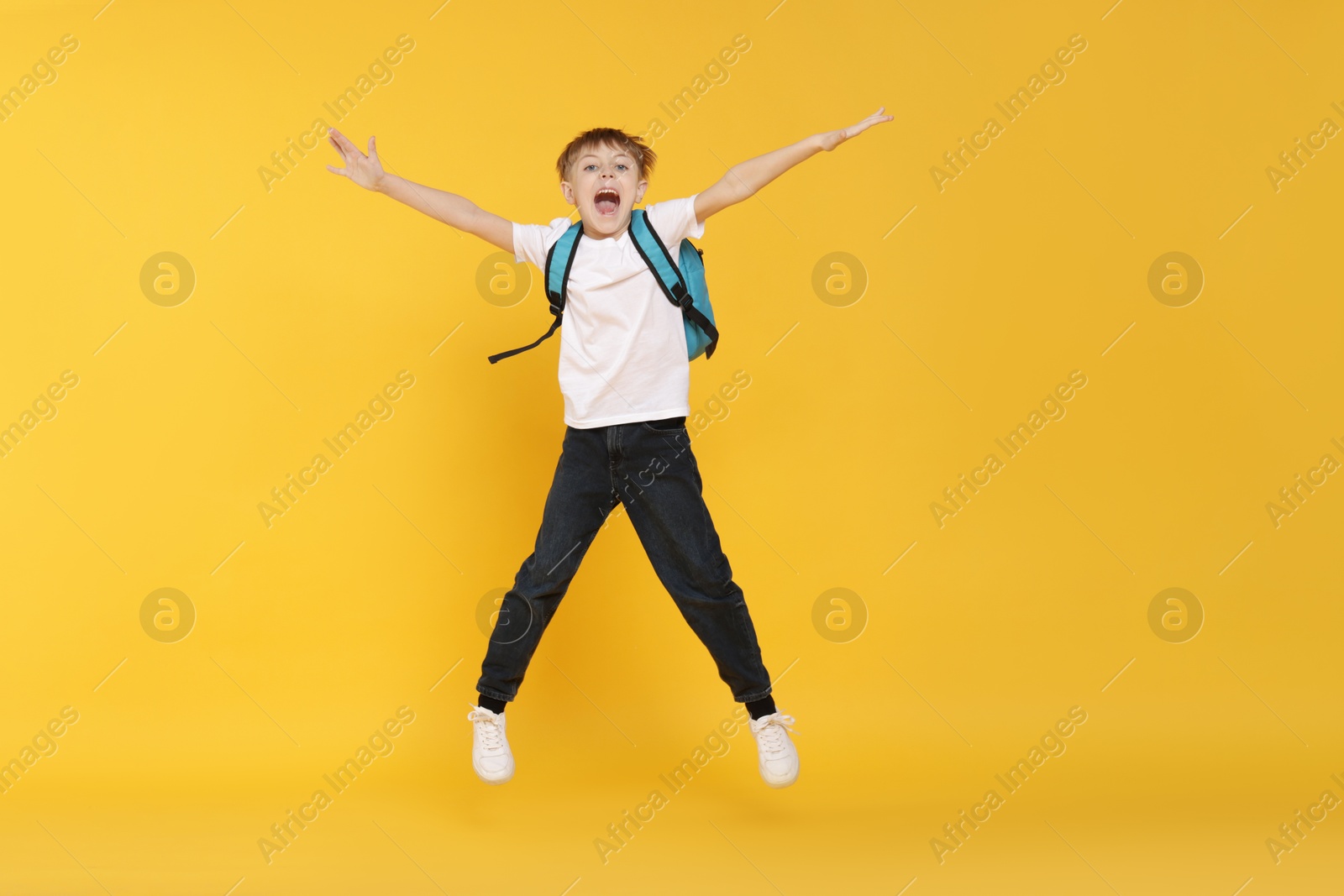 Cute schoolboy with backpack jumping on orange background Photo of Cute schoolboy with backpack jumping on orange background