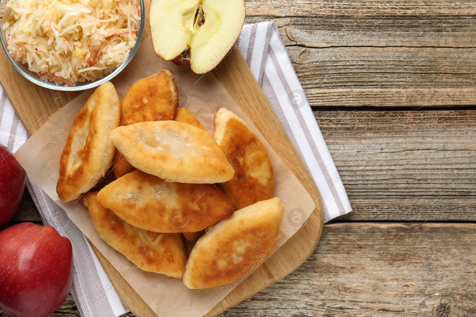 Delicious fried pyrizhky (stuffed pies) and apples on wooden table, flat lay. Space for text Photo of Delicious fried pyrizhky (stuffed pies) and apples on wooden table, flat lay. Space for text