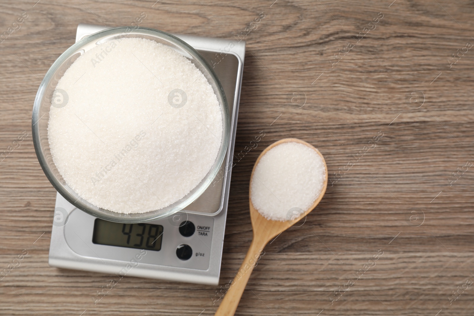 Digital kitchen scale with bowl of sugar and spoon on wooden table, flat lay. Space for text Photo of Digital kitchen scale with bowl of sugar and spoon on wooden table, flat lay. Space for text