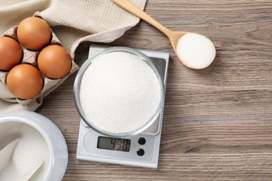 Photo of Digital kitchen scale with bowl of sugar and eggs on wooden table, flat lay