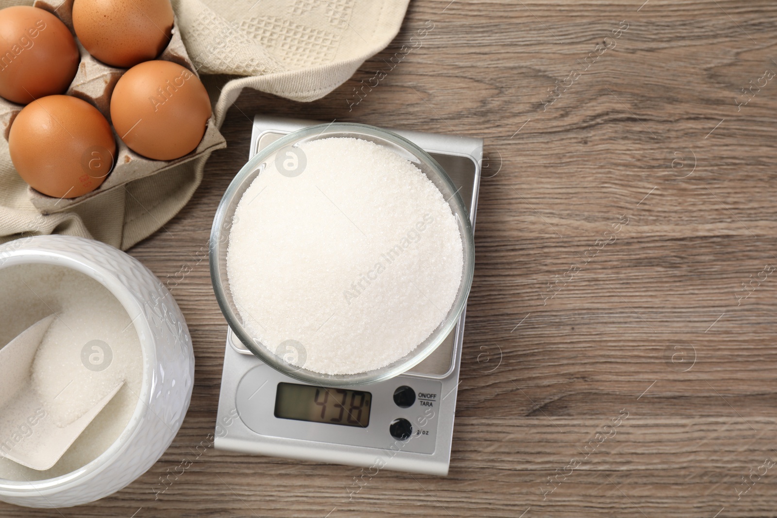 Digital kitchen scale with bowl of sugar and eggs on wooden table, flat lay Photo of Digital kitchen scale with bowl of sugar and eggs on wooden table, flat lay
