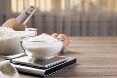 Photo of Digital kitchen scale with bowl of sugar and other products on wooden table indoors, closeup. Space for text