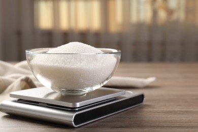 Photo of Digital kitchen scale with bowl of sugar on wooden table indoors, closeup. Space for text