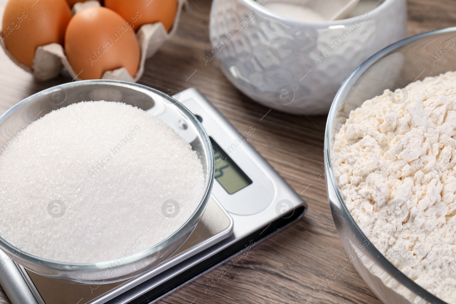 Digital kitchen scale with bowl of sugar and other products on wooden table, closeup Photo of Digital kitchen scale with bowl of sugar and other products on wooden table, closeup