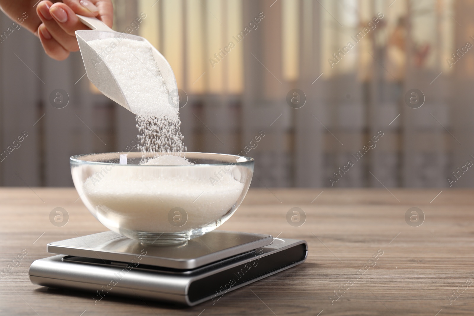 Woman adding sugar into bowl and digital kitchen scale at wooden table indoors, closeup. Space for text Photo of Woman adding sugar into bowl and digital kitchen scale at wooden table indoors, closeup. Space for text