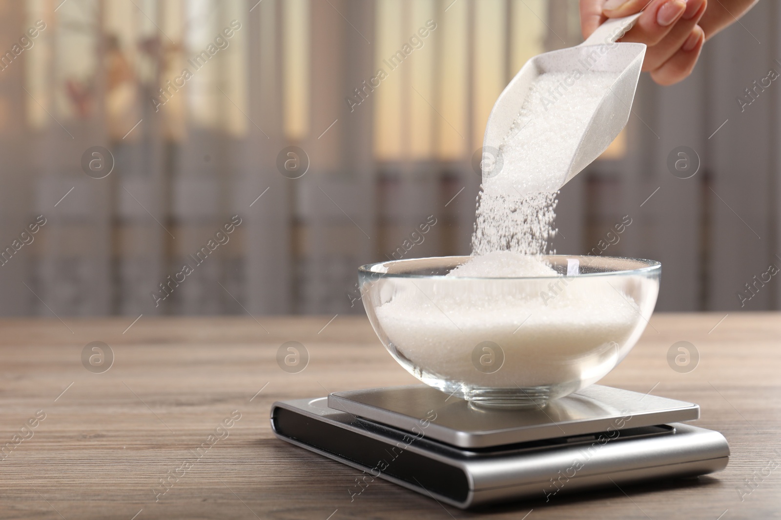 Woman adding sugar into bowl and digital kitchen scale at wooden table indoors, closeup. Space for text Photo of Woman adding sugar into bowl and digital kitchen scale at wooden table indoors, closeup. Space for text