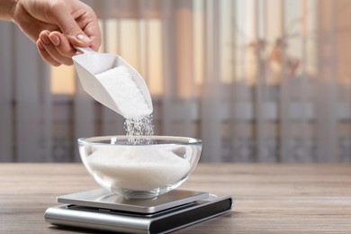 Photo of Woman adding sugar into bowl and digital kitchen scale at wooden table indoors, closeup. Space for text