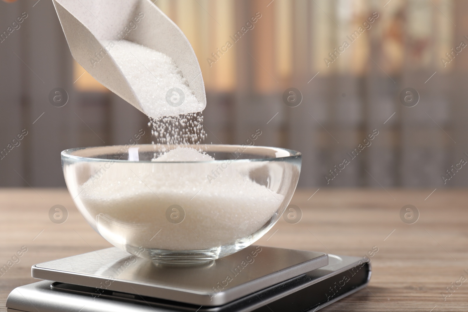 Photo of Adding sugar into bowl on digital kitchen scale at wooden table indoors, closeup. Space for text