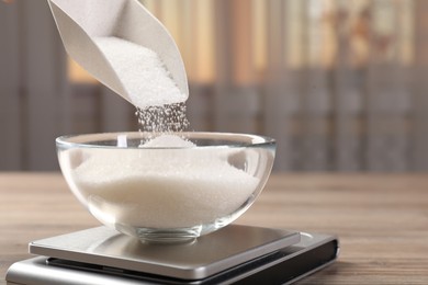 Photo of Adding sugar into bowl on digital kitchen scale at wooden table indoors, closeup. Space for text