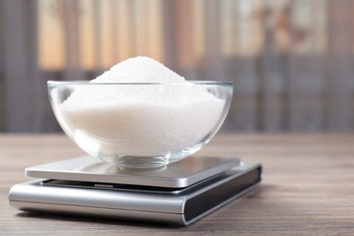 Photo of Digital kitchen scale with bowl of sugar on wooden table indoors, closeup. Space for text