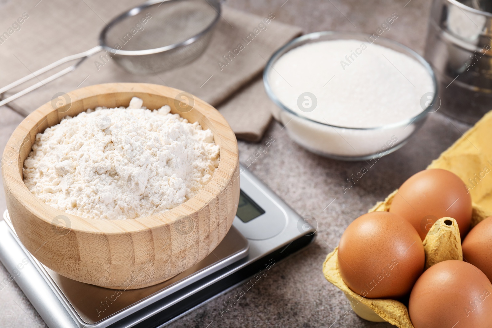 Digital kitchen scale with bowl of flour and other products on grey textured table, closeup Photo of Digital kitchen scale with bowl of flour and other products on grey textured table, closeup