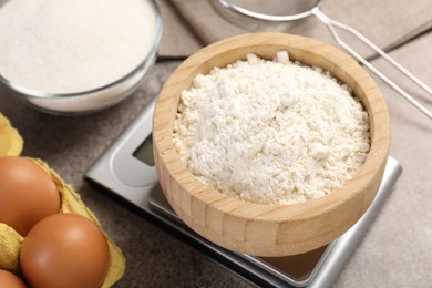 Photo of Digital kitchen scale with bowl of flour and other products on grey textured table, closeup