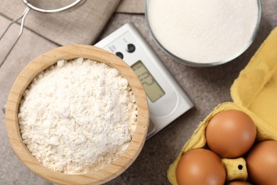 Photo of Digital kitchen scale with bowl of flour and other products on grey textured table, flat lay