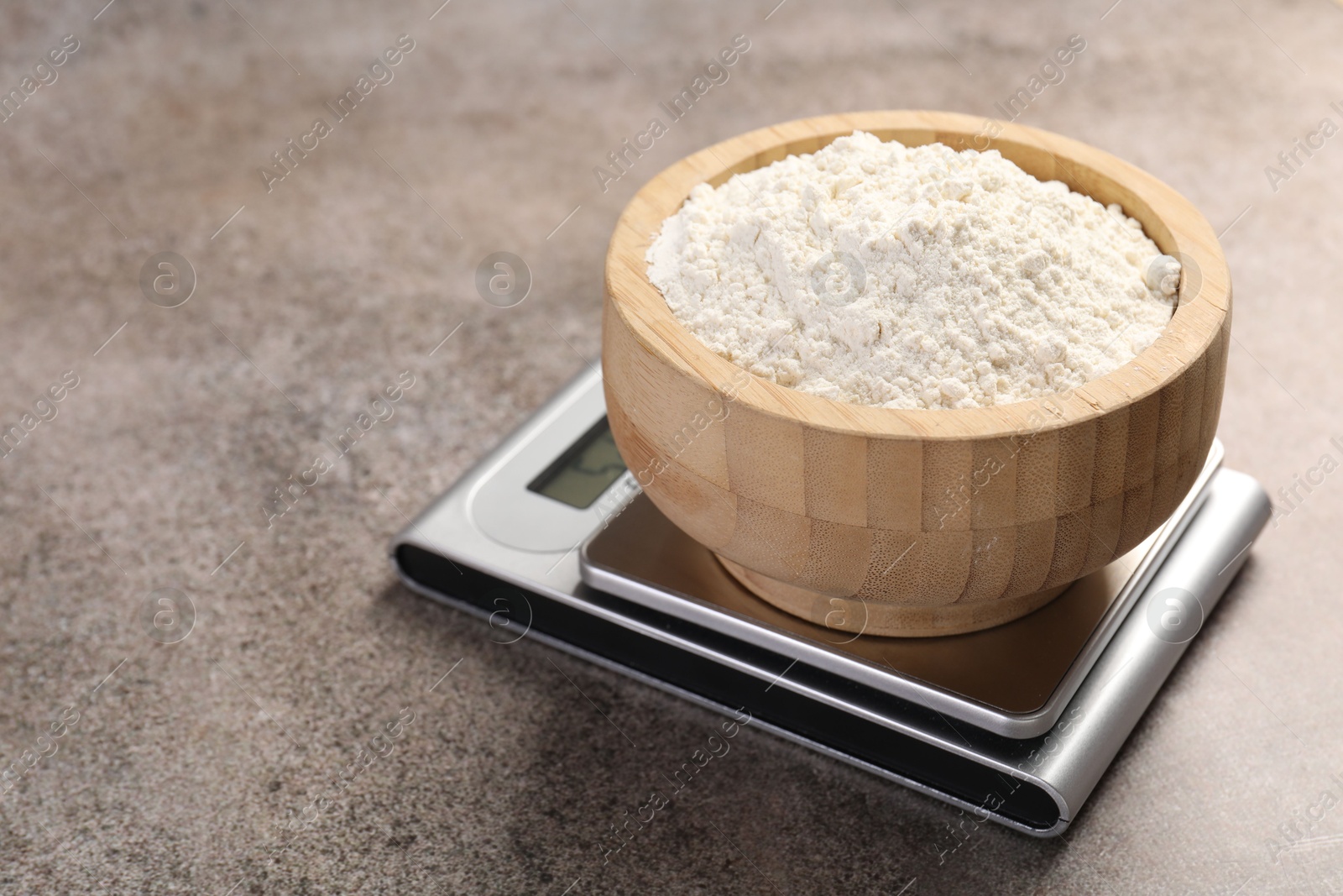 Digital kitchen scale with bowl of flour on grey textured table, closeup Photo of Digital kitchen scale with bowl of flour on grey textured table, closeup
