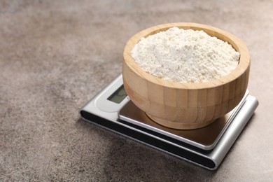 Photo of Digital kitchen scale with bowl of flour on grey textured table, closeup