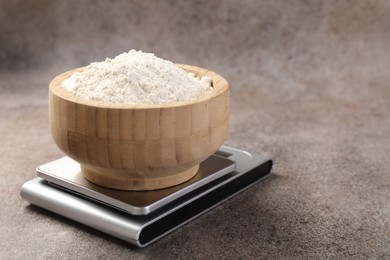 Photo of Digital kitchen scale with bowl of flour on grey textured table, closeup