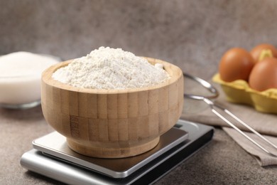 Photo of Digital kitchen scale with bowl of flour on grey textured table, closeup
