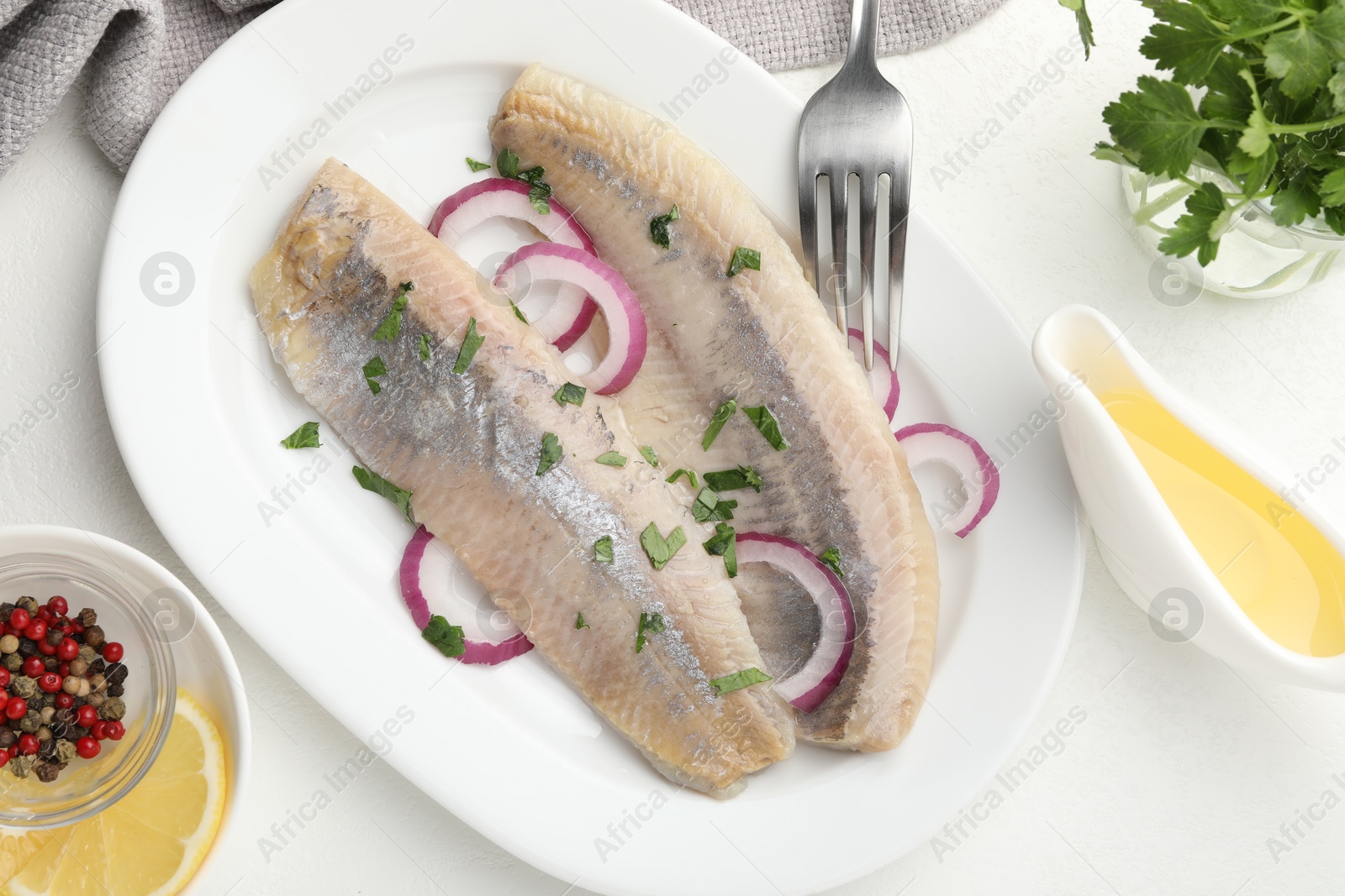 Tasty herring fillets with onions and parsley served on white table, flat lay Photo of Tasty herring fillets with onions and parsley served on white table, flat lay
