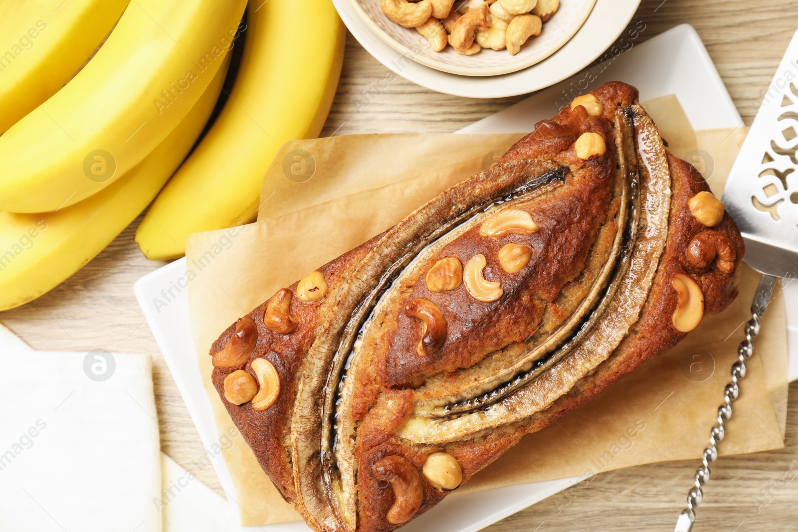 Delicious homemade banana bread with nuts, fruits and server on wooden table, flat lay Photo of Delicious homemade banana bread with nuts, fruits and server on wooden table, flat lay