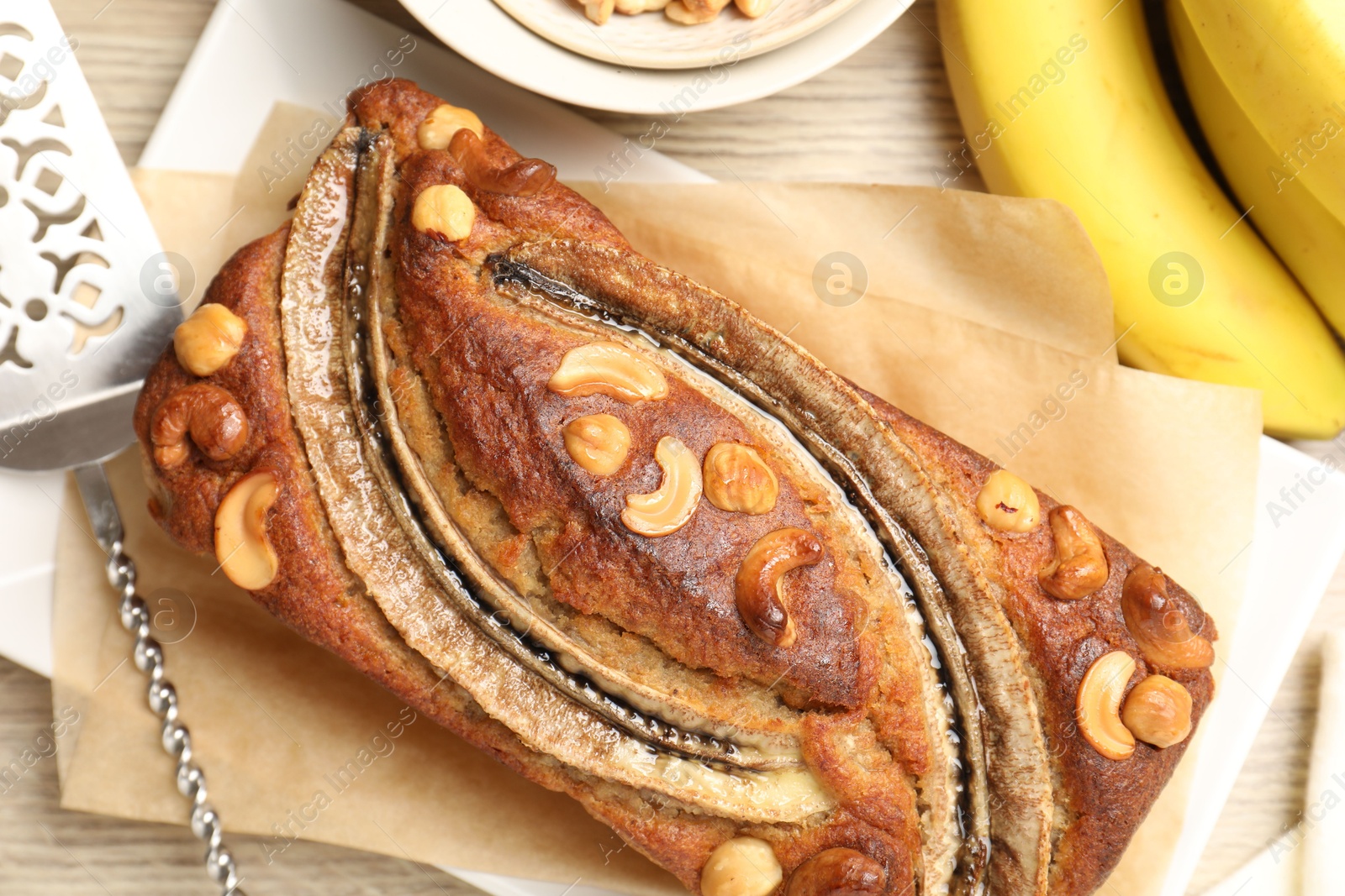Delicious homemade banana bread with nuts, fruits and server on wooden table, flat lay Photo of Delicious homemade banana bread with nuts, fruits and server on wooden table, flat lay