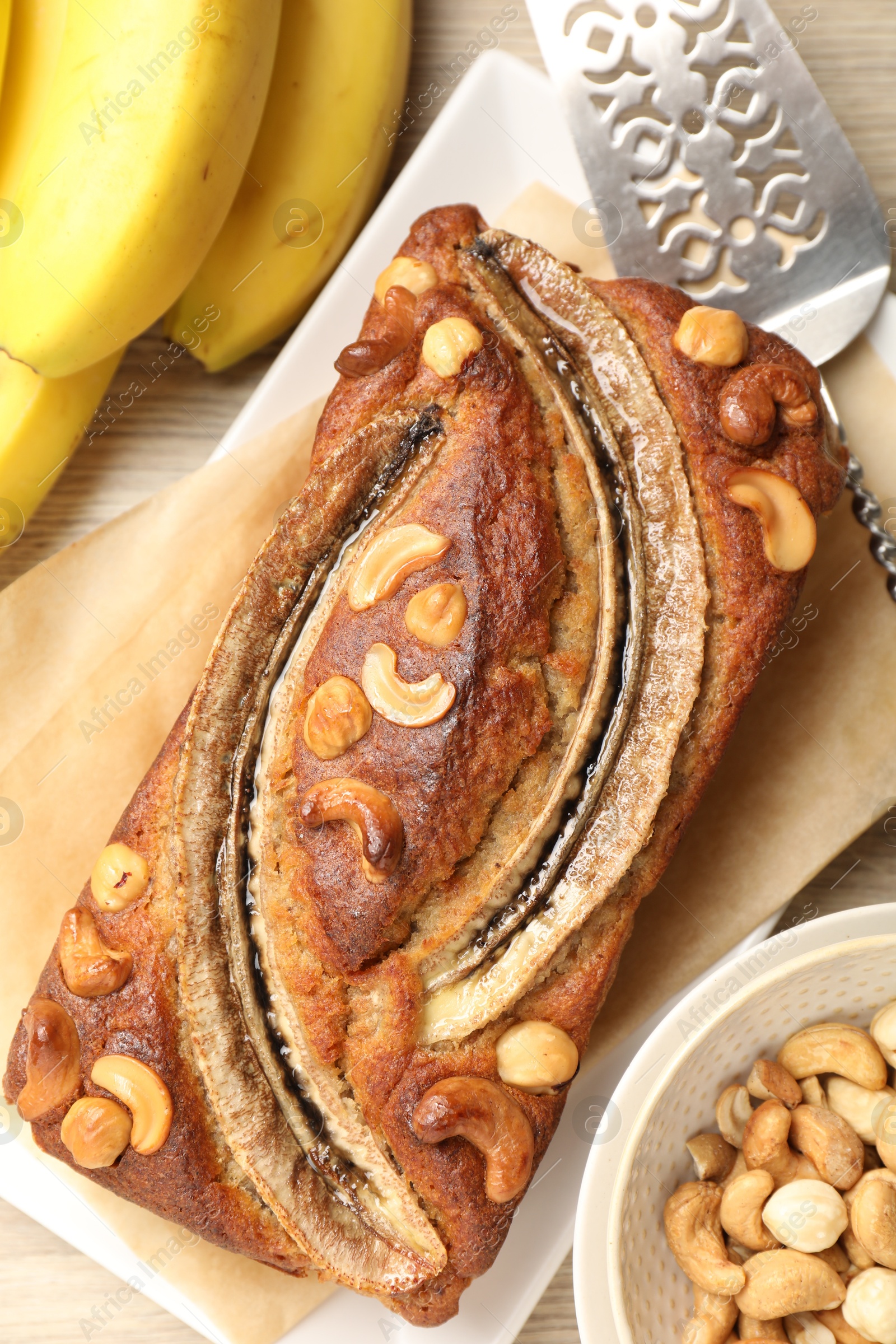 Delicious homemade banana bread with nuts, fruits and server on table, flat lay Photo of Delicious homemade banana bread with nuts, fruits and server on table, flat lay