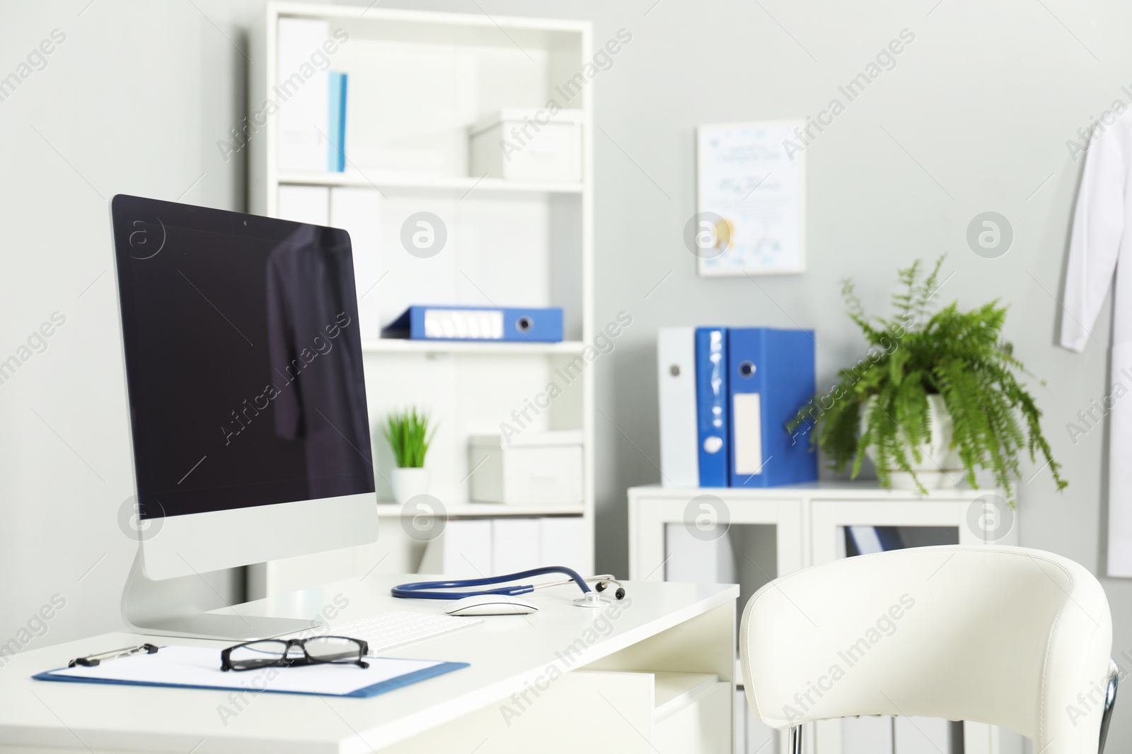 Doctor's workplace. Computer monitor, clipboard, stethoscope and glasses on white table in medical office Photo of Doctor's workplace. Computer monitor, clipboard, stethoscope and glasses on white table in medical office