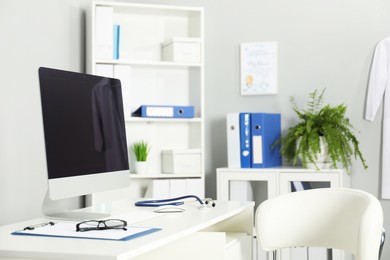 Photo of Doctor's workplace. Computer monitor, clipboard, stethoscope and glasses on white table in medical office