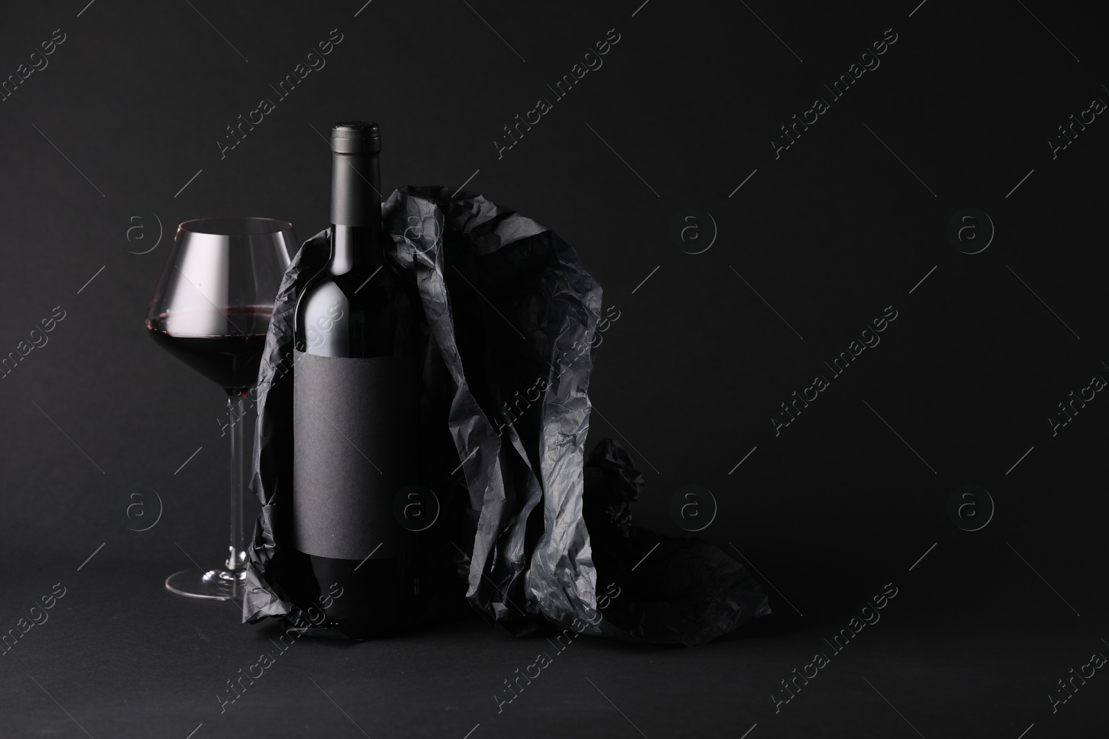 Bottle of wine, wineglass and paper on black background, space for text Photo of Bottle of wine, wineglass and paper on black background, space for text