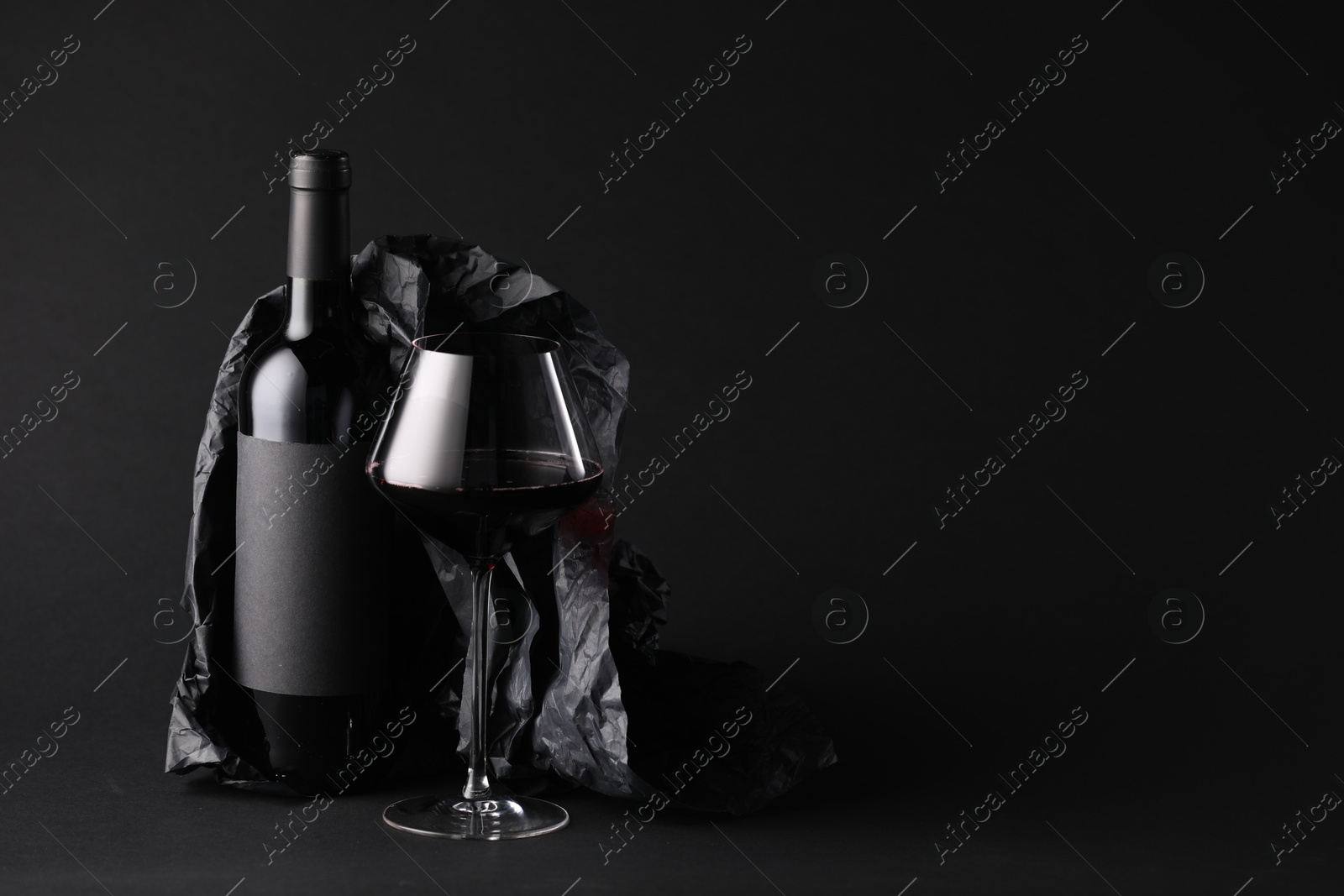 Bottle of wine, wineglass and paper on black background, space for text Photo of Bottle of wine, wineglass and paper on black background, space for text