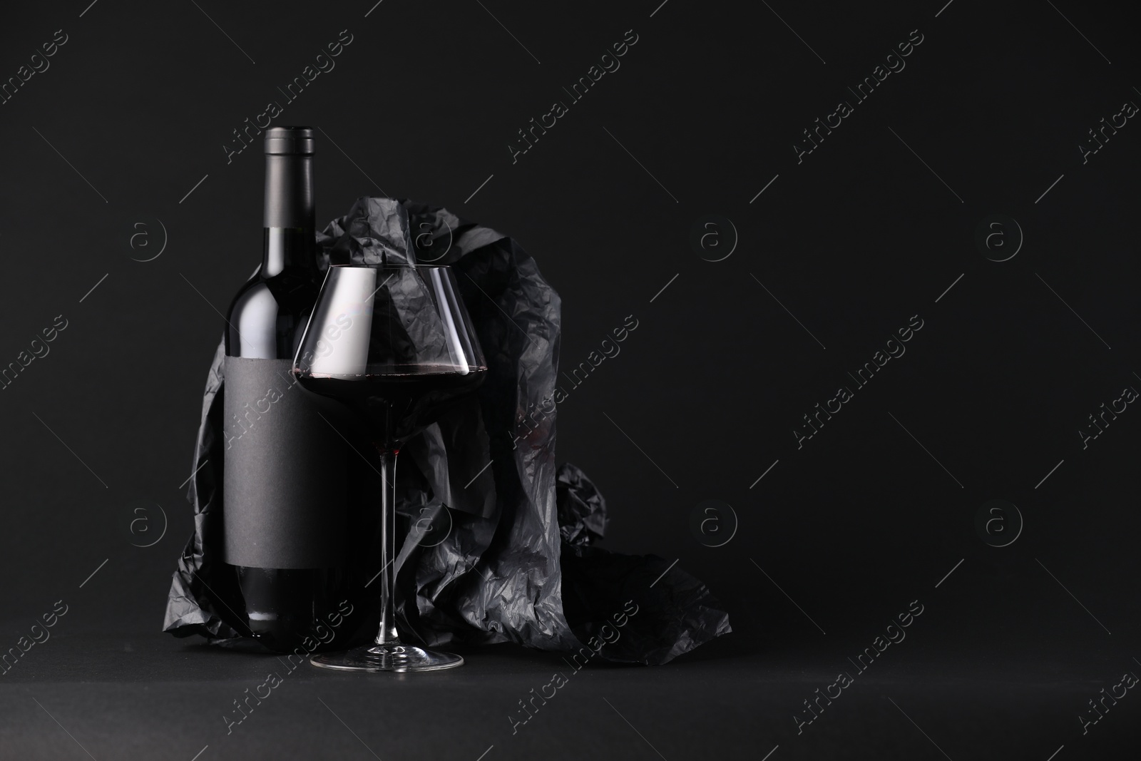 Bottle of wine, wineglass and paper on black background, space for text Photo of Bottle of wine, wineglass and paper on black background, space for text
