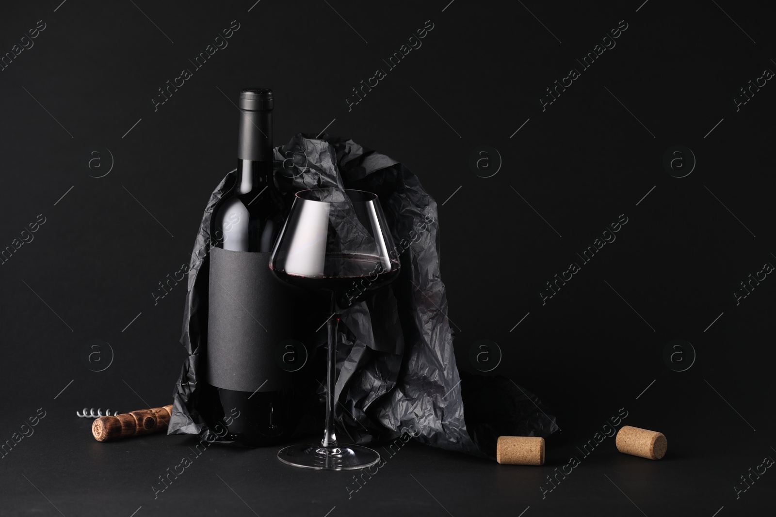 Bottle of wine, wineglass, corkscrew and paper on black background, space for text Photo of Bottle of wine, wineglass, corkscrew and paper on black background, space for text