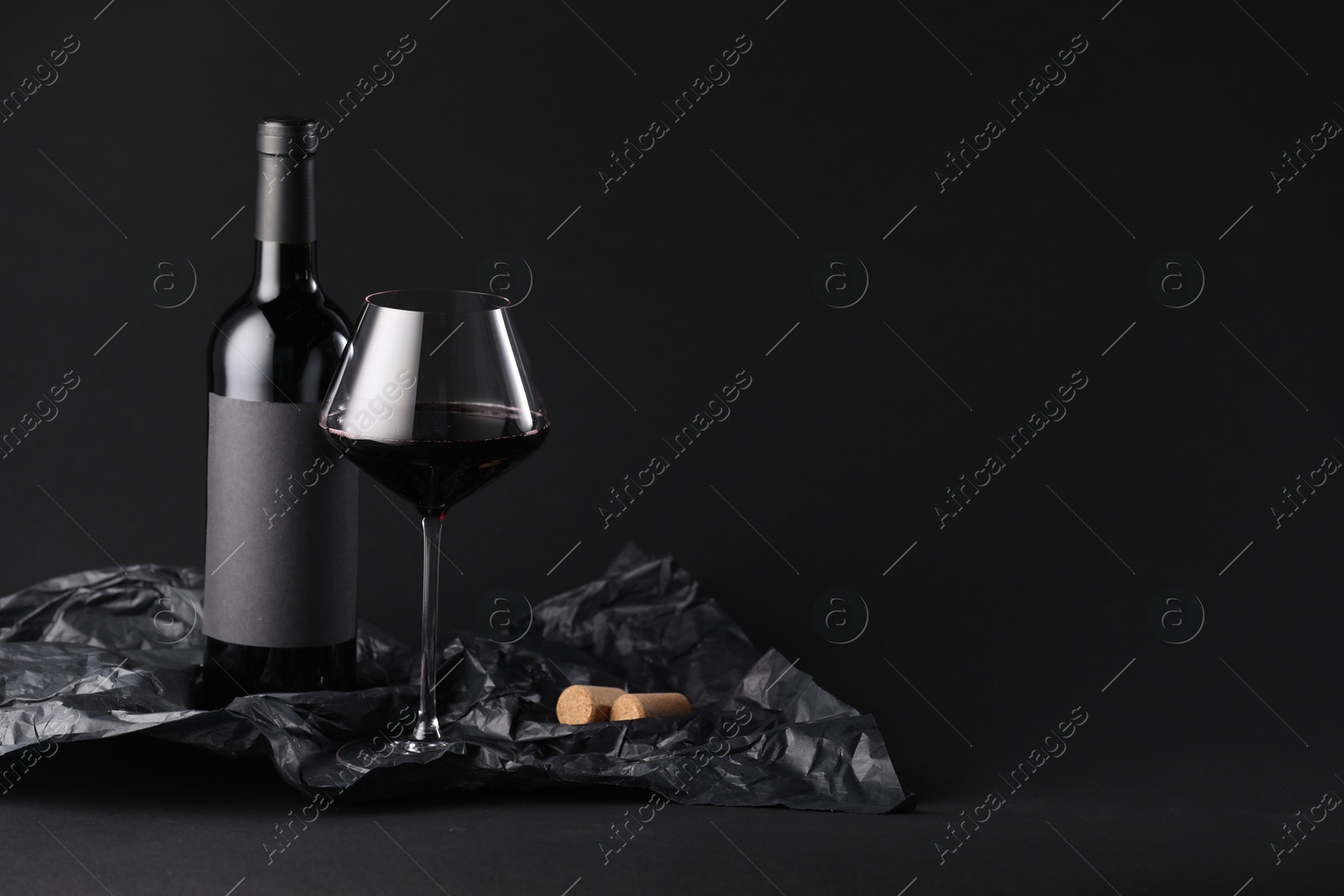 Bottle of wine, wineglass and paper on black background, space for text Photo of Bottle of wine, wineglass and paper on black background, space for text