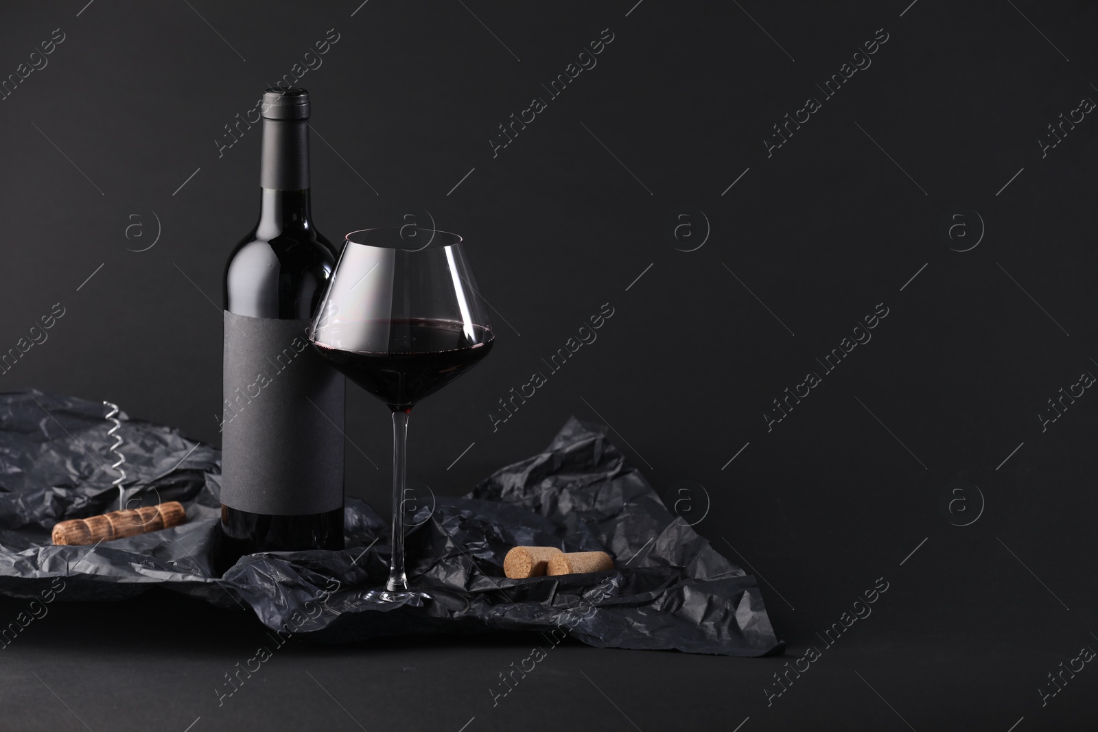 Bottle of wine, wineglass, corkscrew and paper on black background, space for text Photo of Bottle of wine, wineglass, corkscrew and paper on black background, space for text