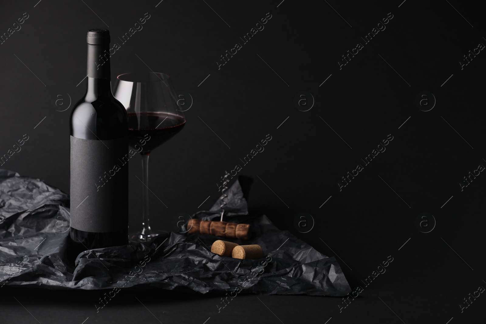Bottle of wine, wineglass, corkscrew and paper on black background, space for text Photo of Bottle of wine, wineglass, corkscrew and paper on black background, space for text
