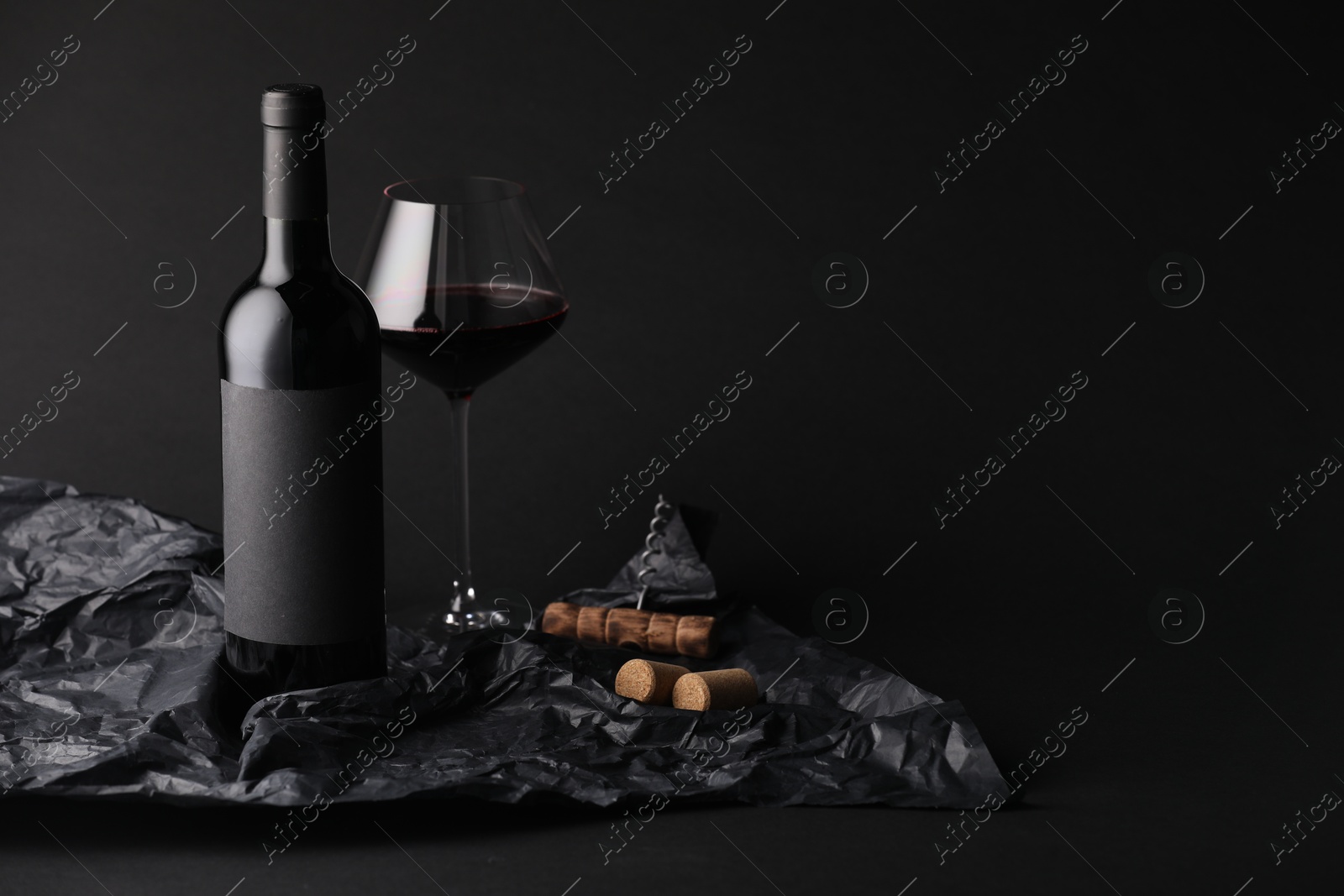 Bottle of wine, wineglass, corkscrew and paper on black background, space for text Photo of Bottle of wine, wineglass, corkscrew and paper on black background, space for text