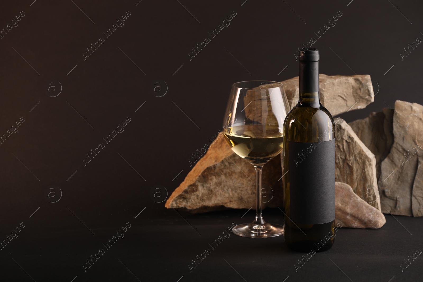 Bottle of wine, wineglass and rocks on black background, space for text Photo of Bottle of wine, wineglass and rocks on black background, space for text