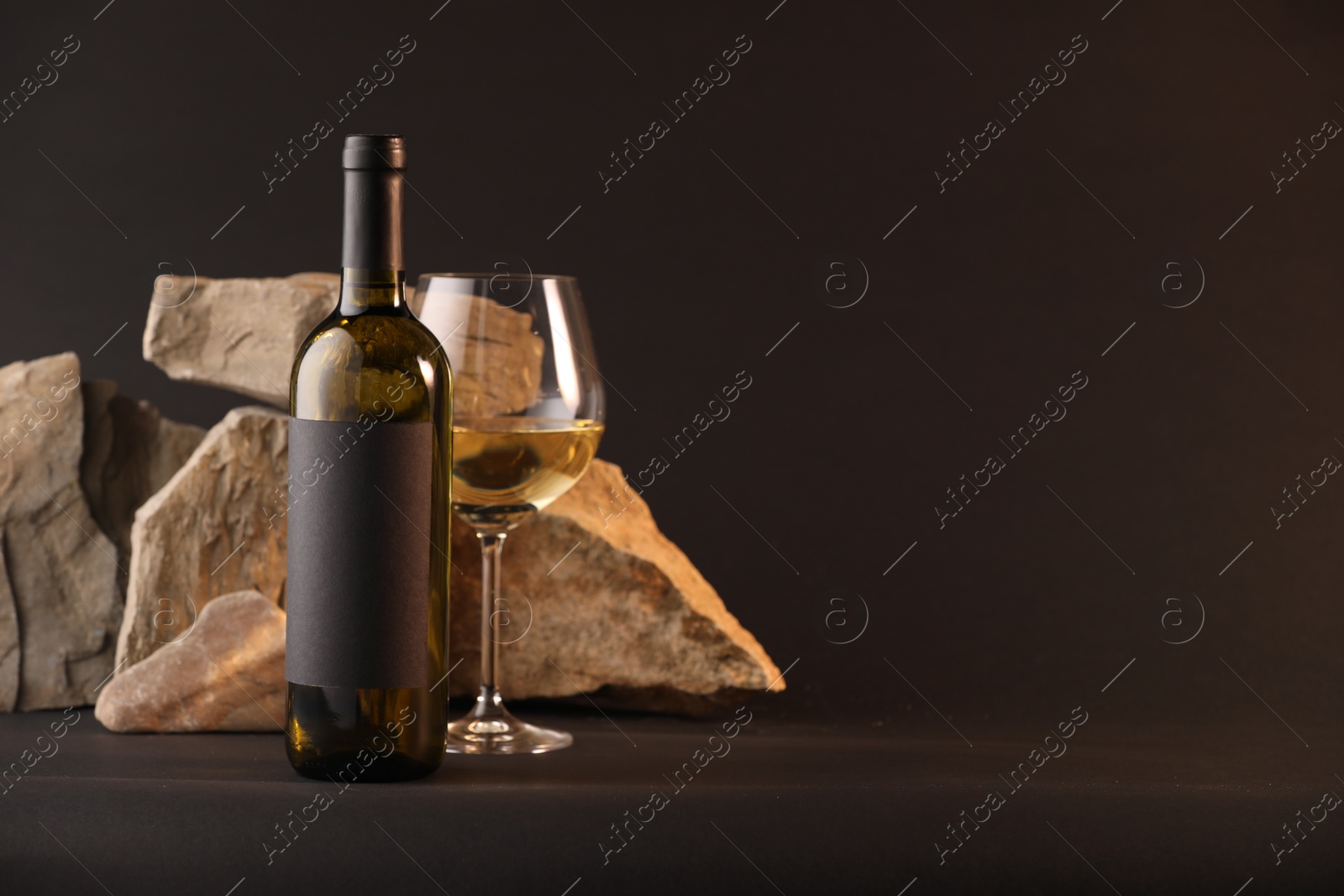 Bottle of wine, wineglass and rocks on black background, space for text Photo of Bottle of wine, wineglass and rocks on black background, space for text