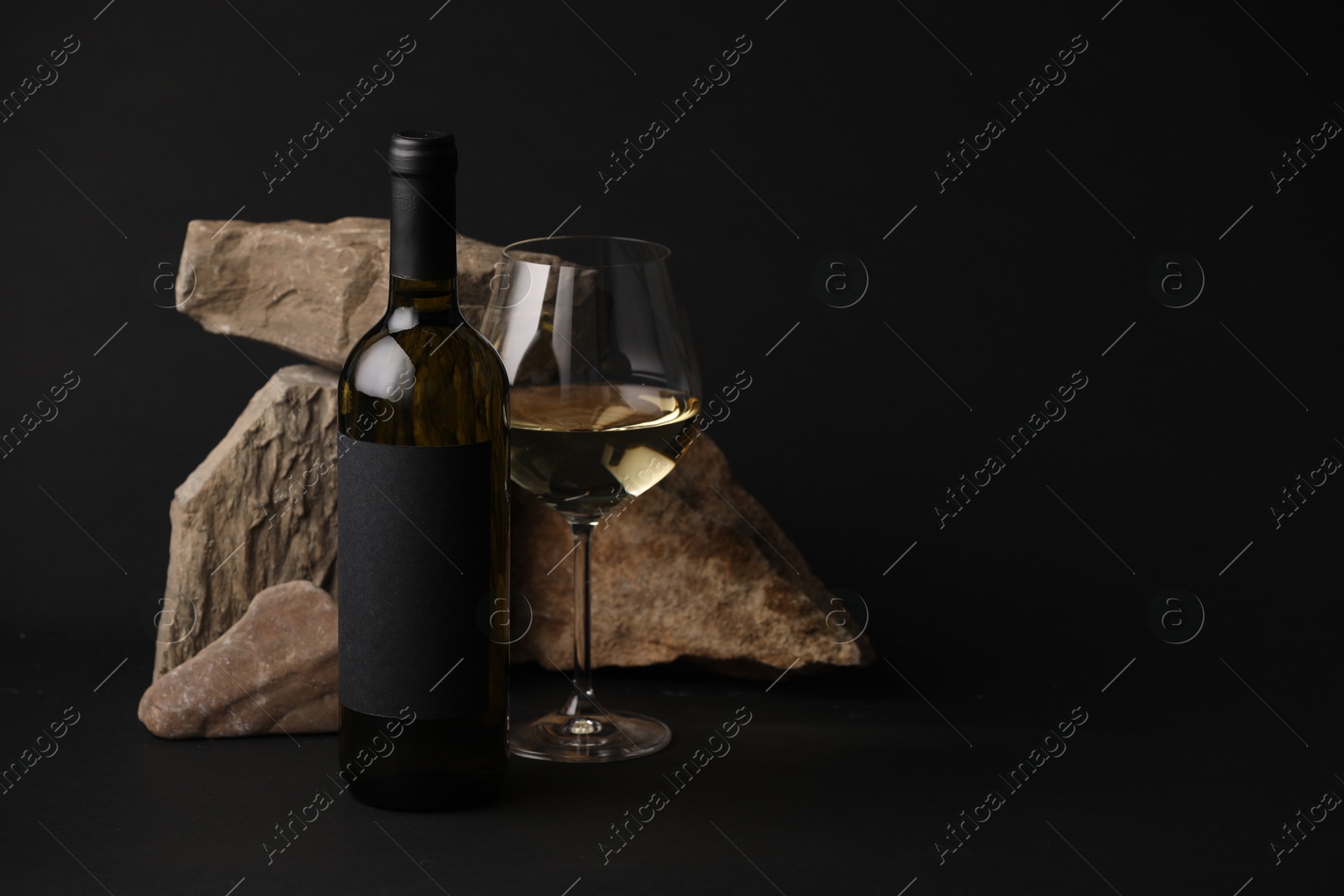 Bottle of wine, wineglass and rocks on black background, space for text Photo of Bottle of wine, wineglass and rocks on black background, space for text
