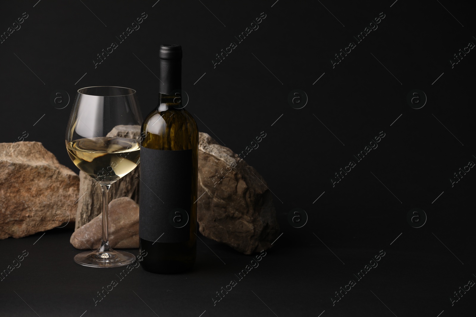 Bottle of wine, wineglass and rocks on black background, space for text Photo of Bottle of wine, wineglass and rocks on black background, space for text