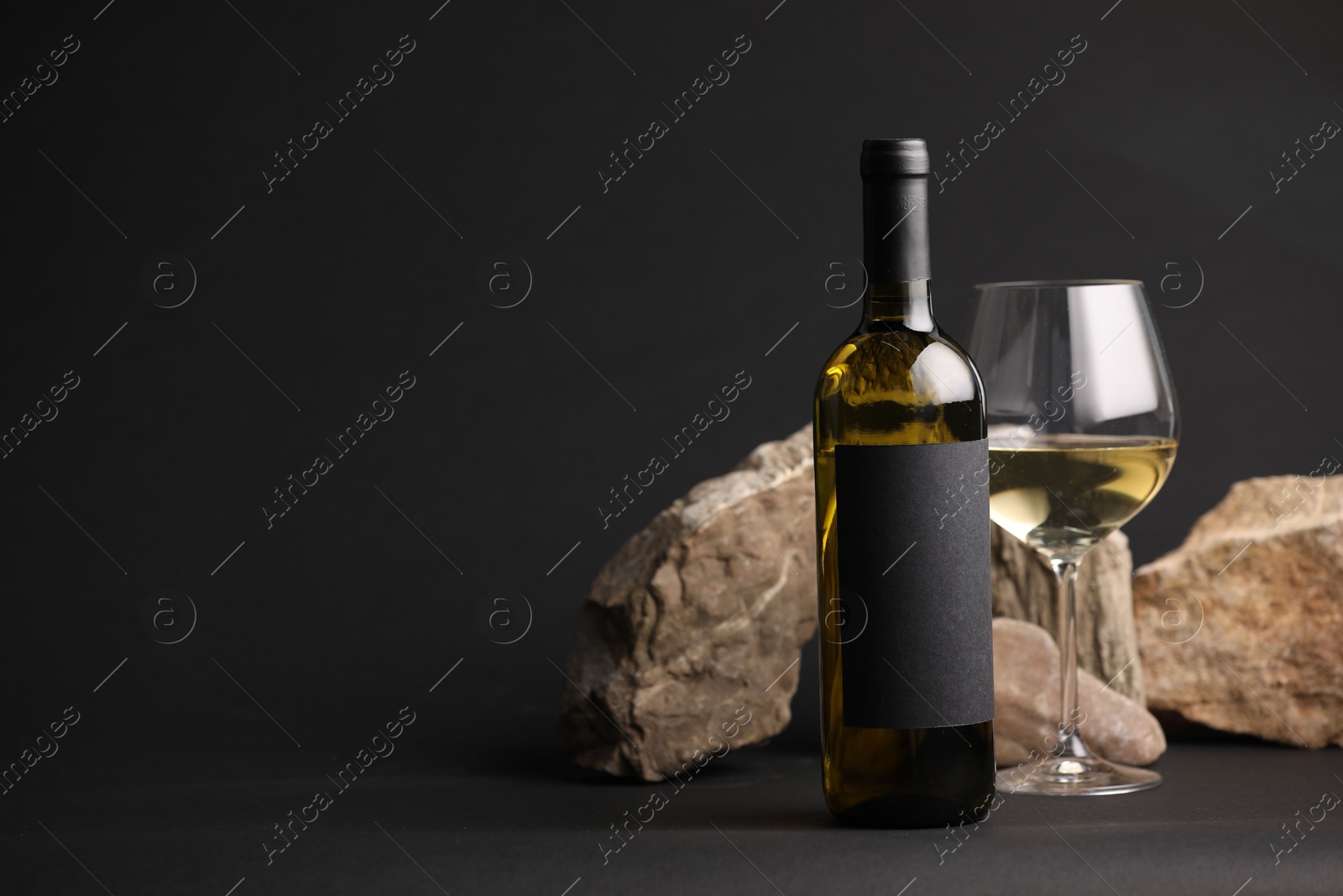 Bottle of wine, wineglass and rocks on black background, space for text Photo of Bottle of wine, wineglass and rocks on black background, space for text