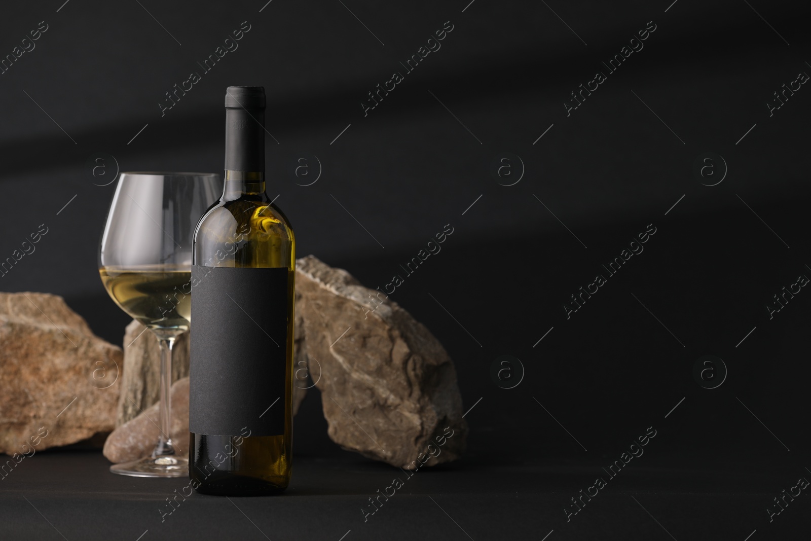 Bottle of wine, wineglass and rocks on black background, space for text Photo of Bottle of wine, wineglass and rocks on black background, space for text