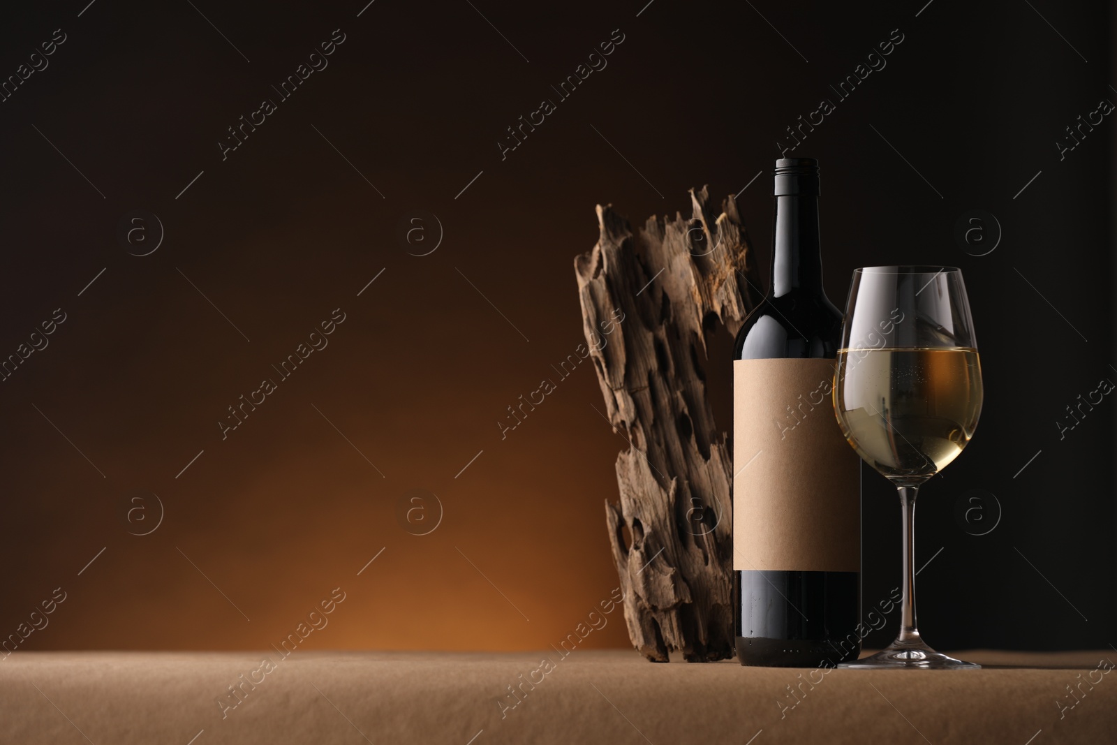 Bottle of wine, tree bark and wineglass on brown table against dark background, space for text Photo of Bottle of wine, tree bark and wineglass on brown table against dark background, space for text
