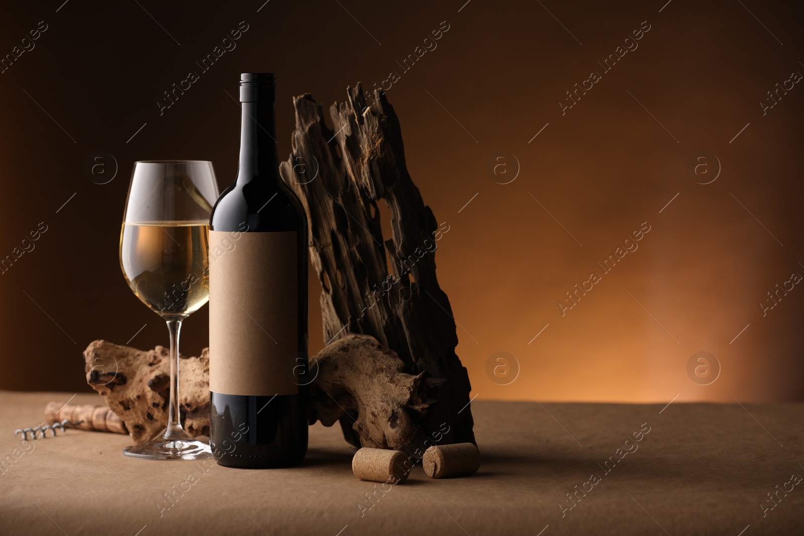 Bottle of wine, tree bark and wineglass on brown table against dark background, space for text Photo of Bottle of wine, tree bark and wineglass on brown table against dark background, space for text