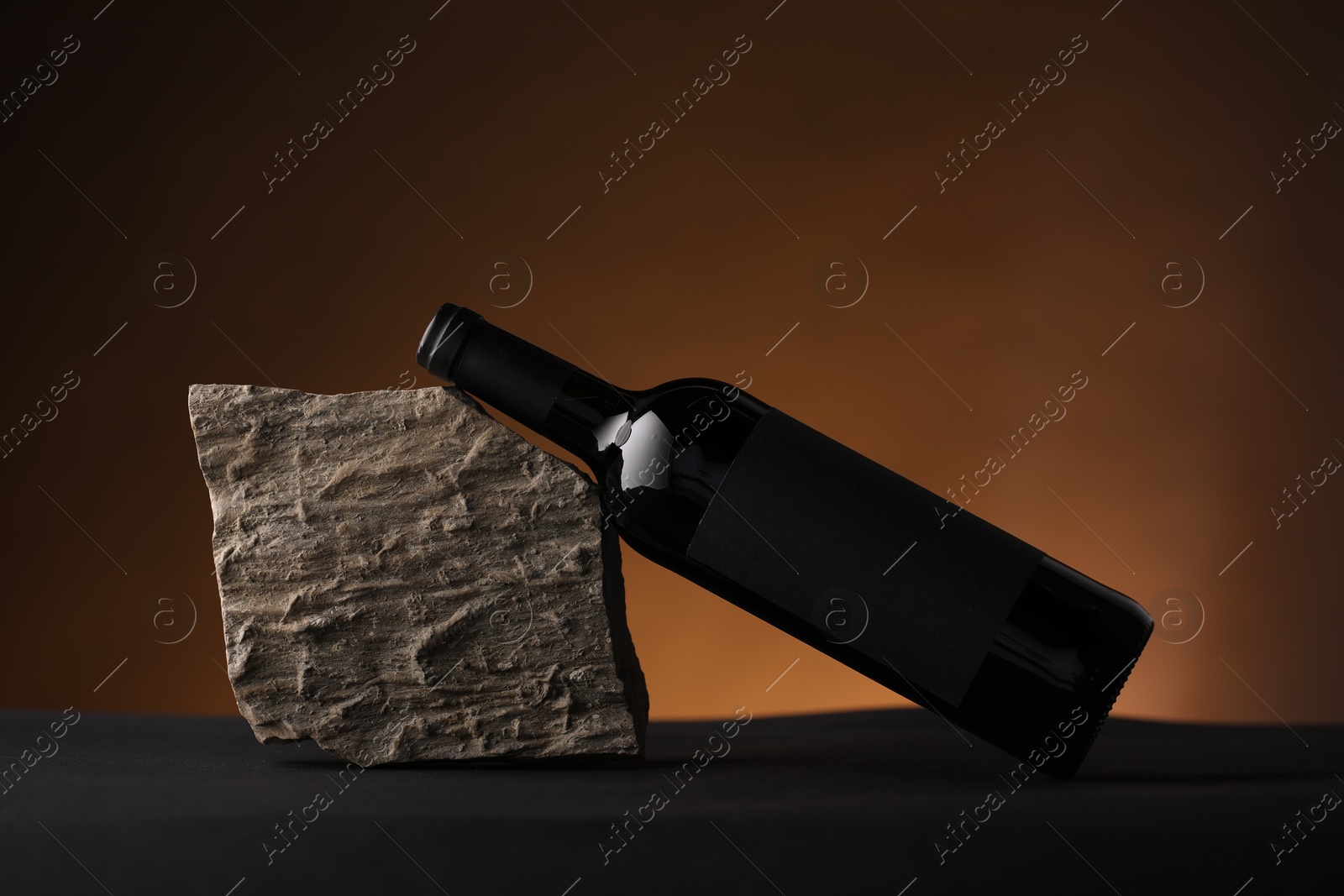 Bottle of wine and rock on black table against dark brown background Photo of Bottle of wine and rock on black table against dark brown background