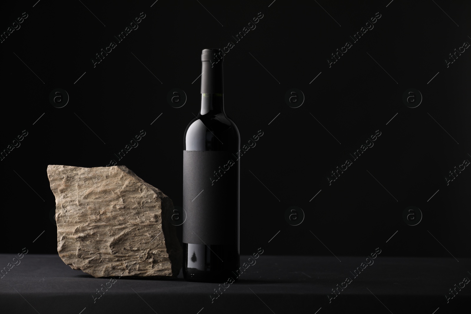 Bottle of wine and rock on black table, space for text Photo of Bottle of wine and rock on black table, space for text